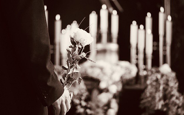 Рука с белой розой на фоне свечей